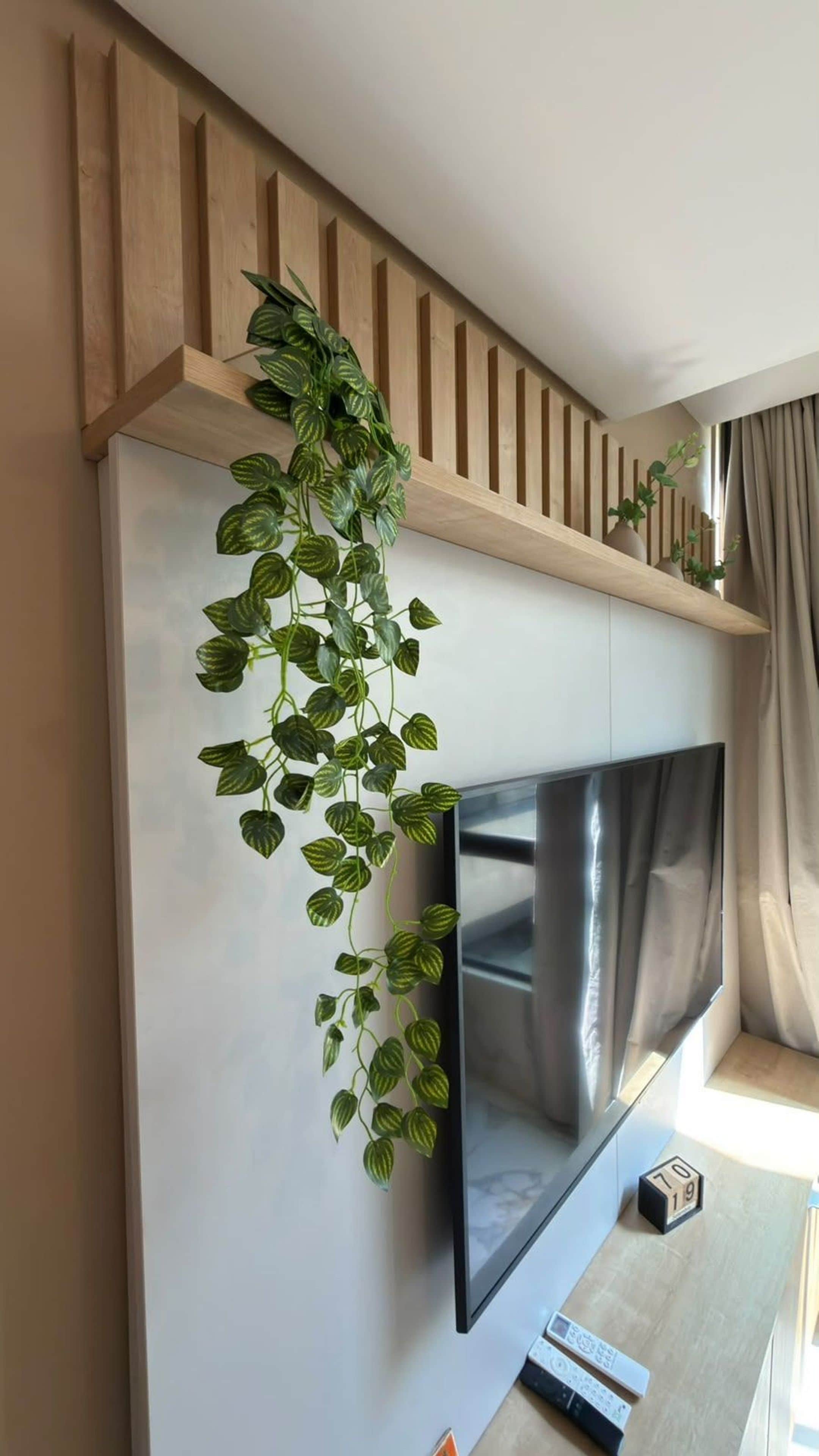 A flat-screen TV mounted on a wall with a wooden shelf above it.