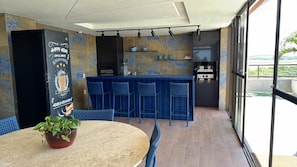A modern kitchen with a bar area, a dining table with chairs, and a potted plant.