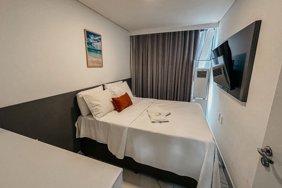 A hotel room with a bed, a flat-screen TV, a painting, and a window with curtains.
