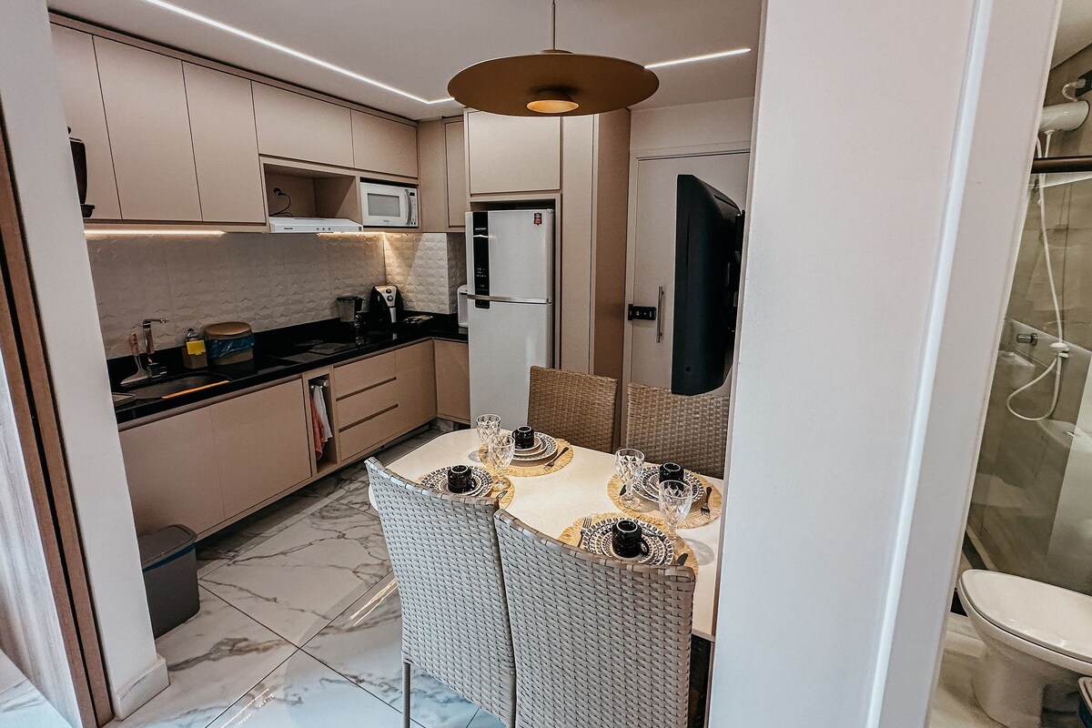 Una cocina compacta con electrodomésticos modernos, un comedor con sillas de mimbre y una zona de ducha visible.