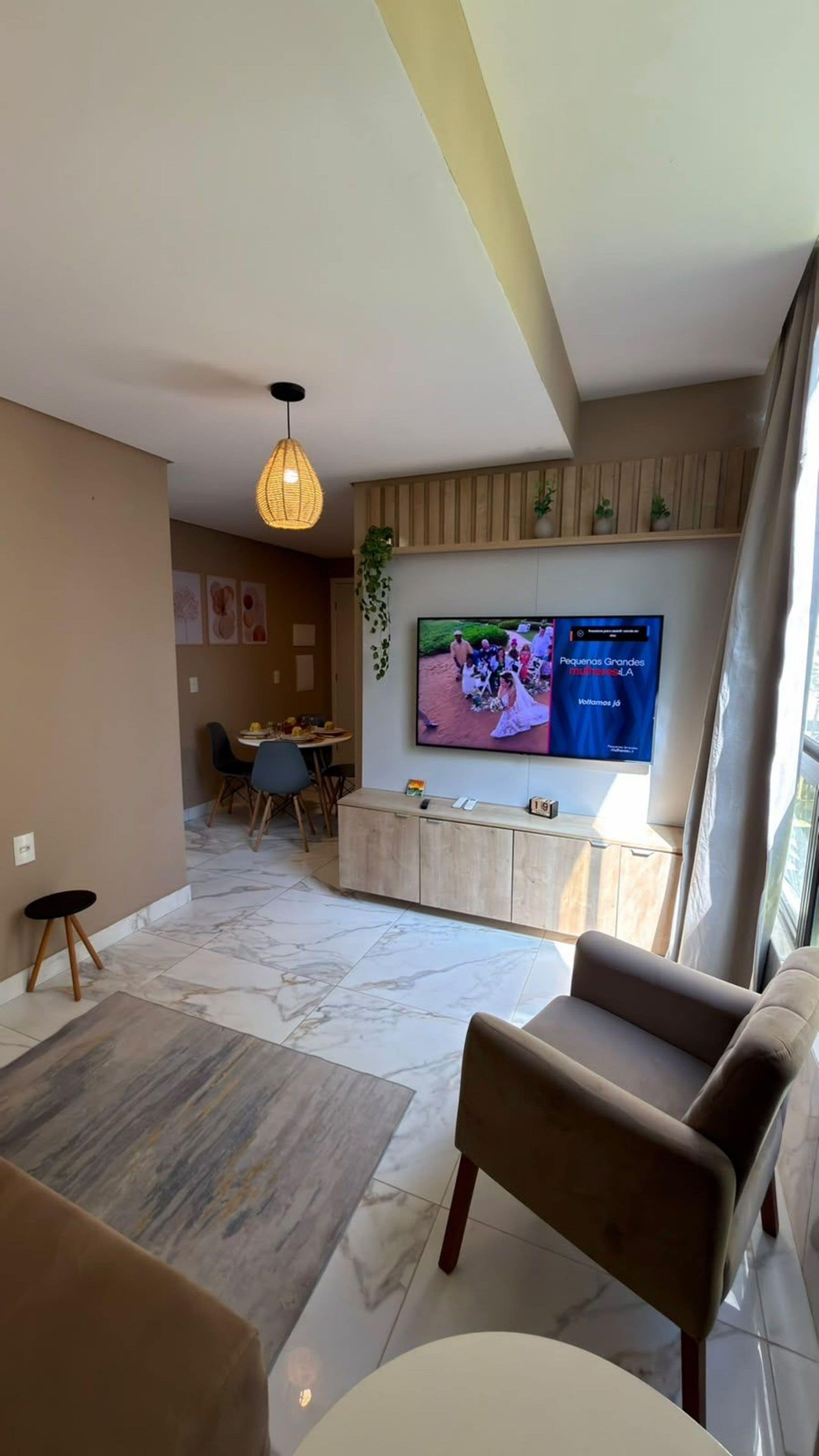A modern living room with a flat-screen TV mounted on the wall, a sofa, a coffee table, and a dining area in the background.