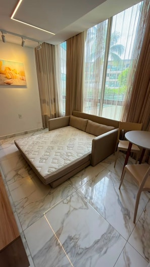 A modern living room with a sofa, a dining table, and a large window with curtains. - Porto Atlantis (Ipojuca)