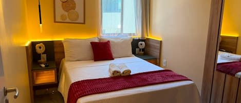 A hotel room with a bed, bedside tables, a window with curtains, and a wall-mounted artwork.