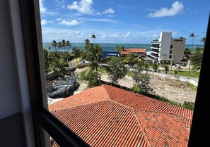 A view from a window overlooking a beach with palm trees, a sandy area, and buildings in the background.