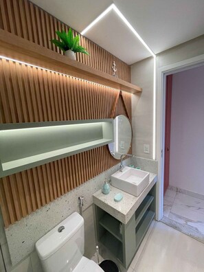 A modern bathroom with a wooden slat wall, a large mirror, two sinks, and a toilet. - Porto Atlantis (Ipojuca)