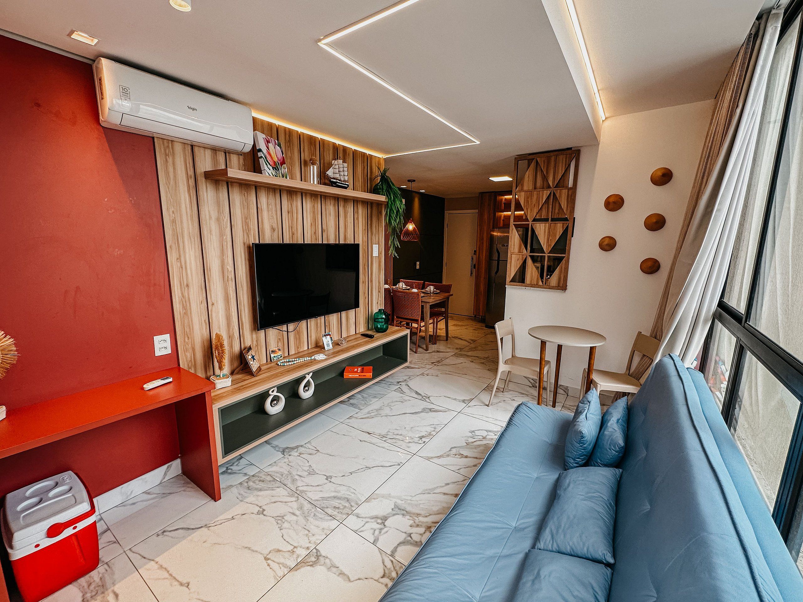 Ein modernes Wohnzimmer mit Flachbildfernseher, einer Wandpaneele aus Holz und einem blauen Sofa.