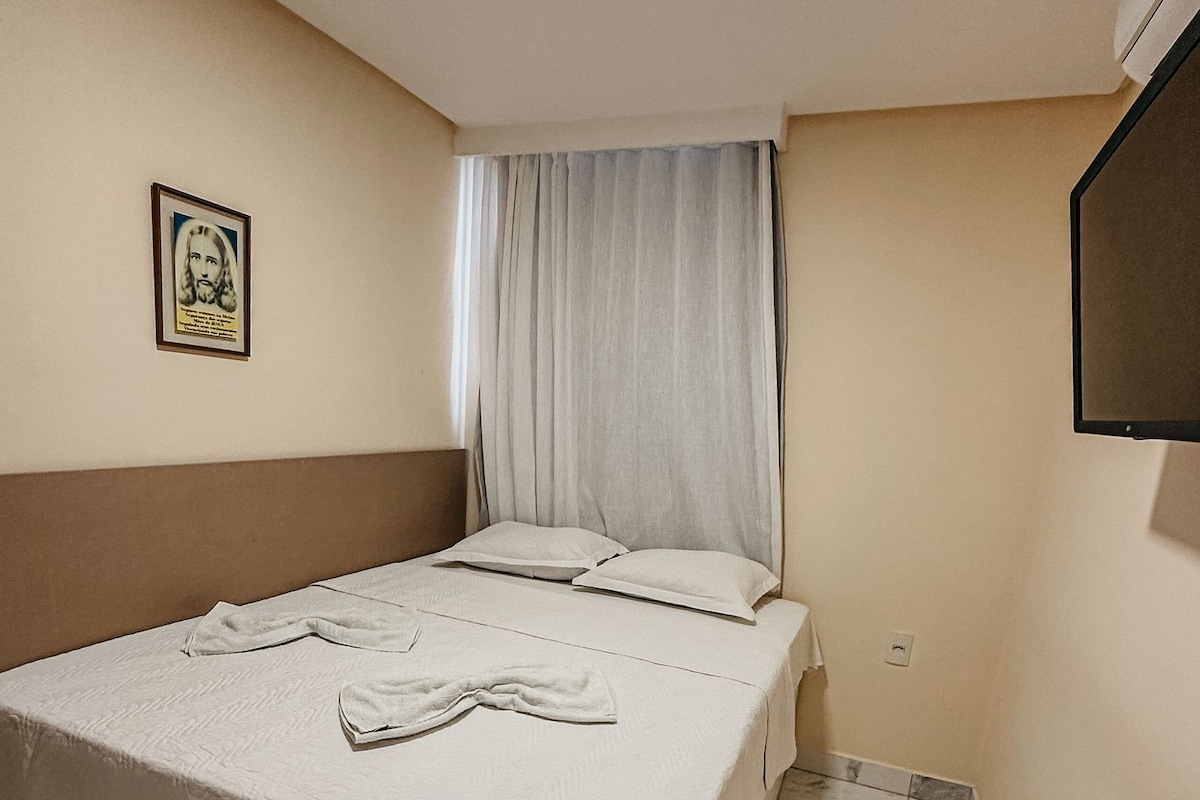 A neatly made bed with a white bedspread and pillows, a framed picture on the wall, and a tiled floor.