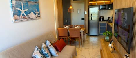 Una sala de estar con sofá, mesa de comedor, sillas y una cocina con refrigerador y microondas.