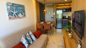 Una sala de estar con sofá, mesa de comedor, sillas y una cocina con refrigerador y microondas.