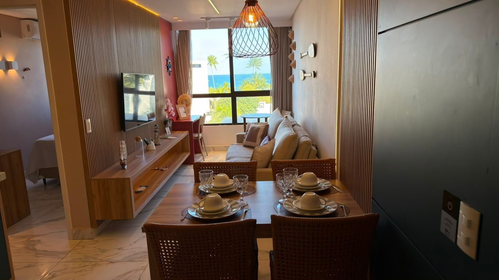 Uma área de refeições com uma mesa comprida posta para quatro pessoas, um sofá e vista para o oceano.