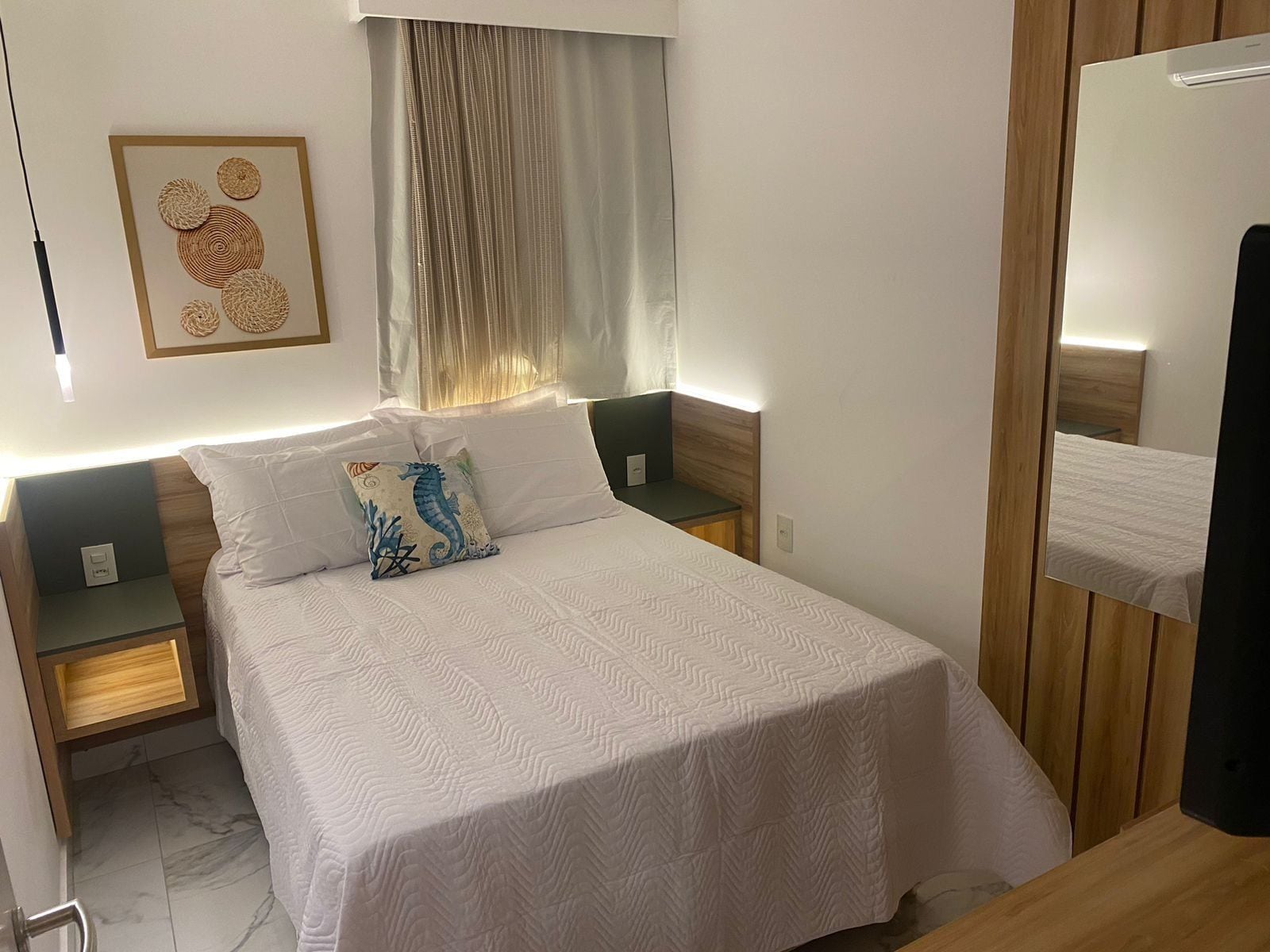 Quarto bem organizado com uma cama grande, duas mesas de cabeceira, uma obra de arte pendurada na parede e um espelho.