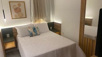 Quarto bem organizado com uma cama grande, duas mesas de cabeceira, uma obra de arte pendurada na parede e um espelho.