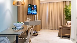 A modern living room with a flat-screen TV mounted on the wall, a dining area with a glass table, and a seating area with a sofa.