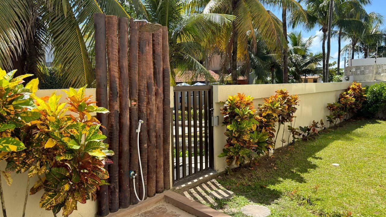 A gated entrance with a wooden gate, a concrete wall, and a grassy area with plants.