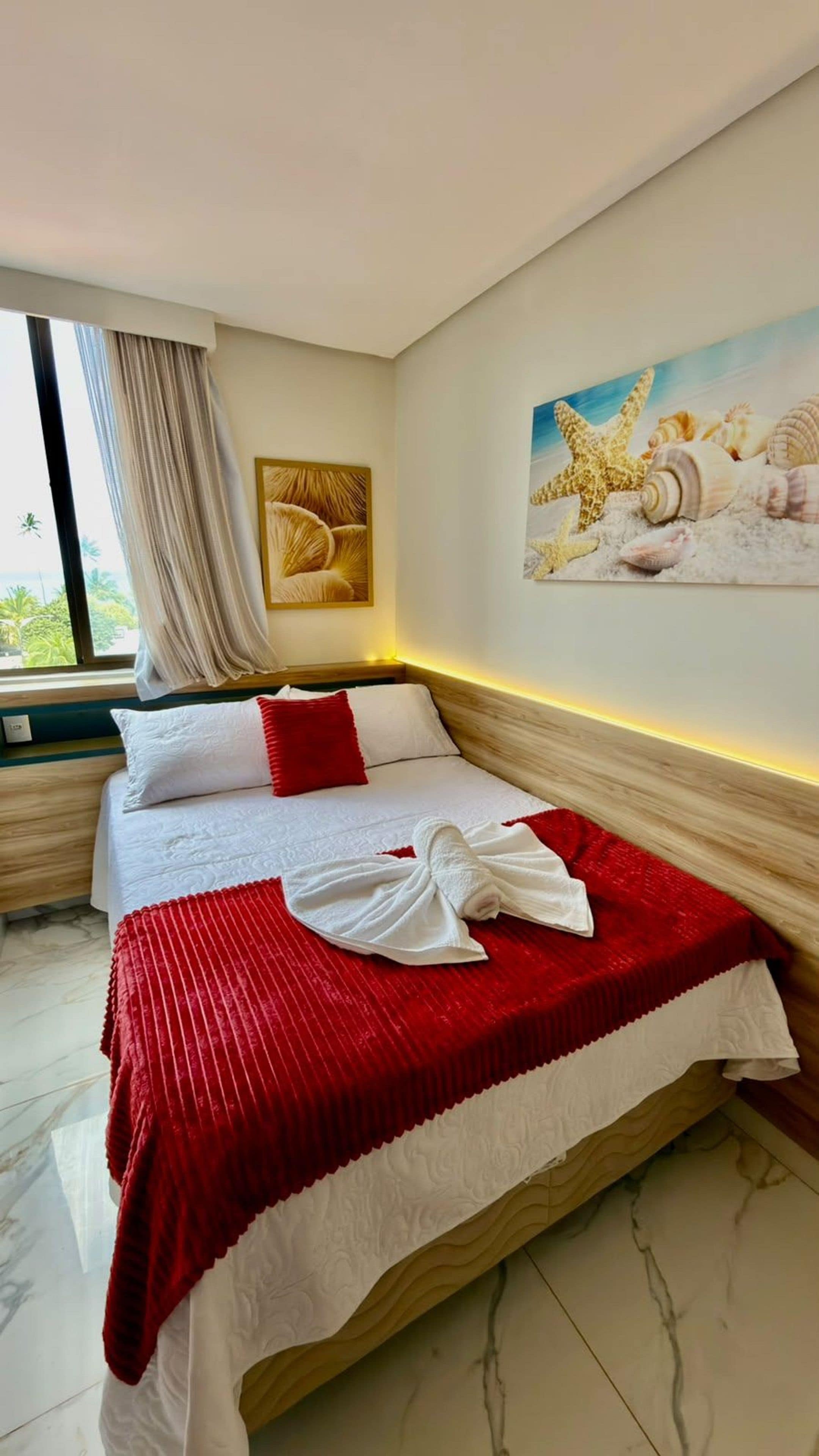 Une chambre d’hôtel avec un lit, un tableau représentant des coquillages et une fenêtre avec des rideaux.