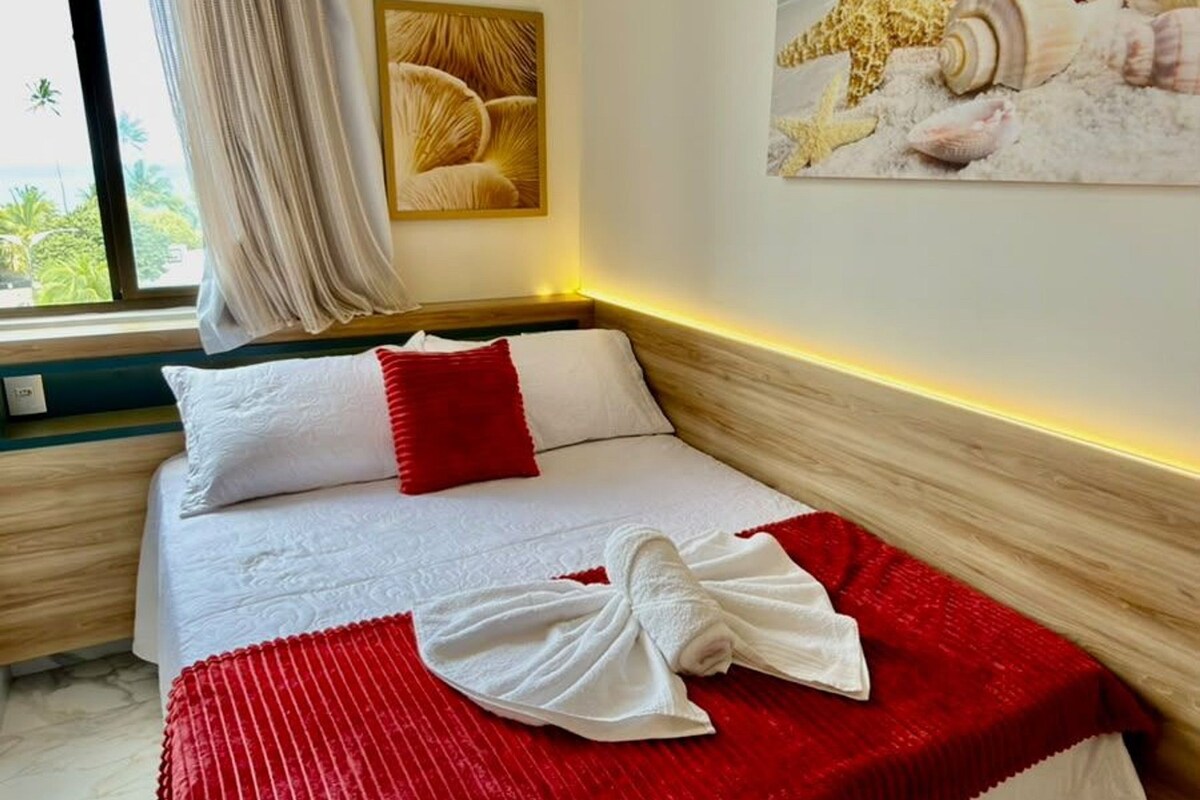 A hotel room with a bed, a painting of seashells, and a window with curtains.