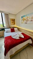 Habitación de hotel con cama, un cuadro de conchas marinas y una ventana con cortinas.