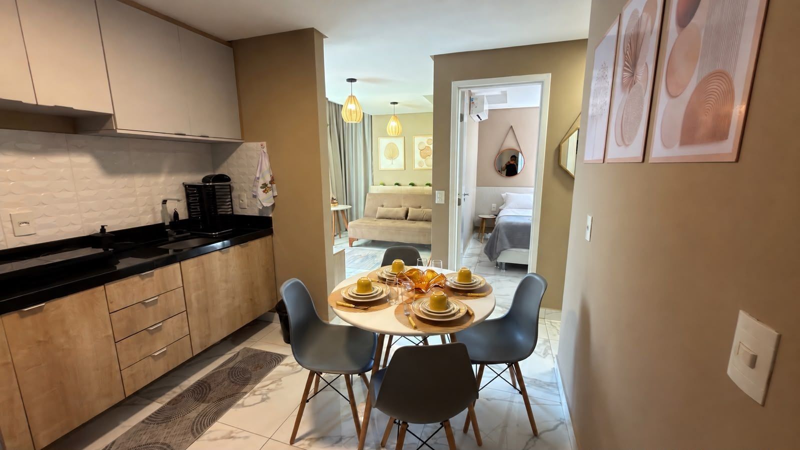 A modern kitchen with a dining area, featuring a round table with chairs, a coffee machine, and a view into the living room.