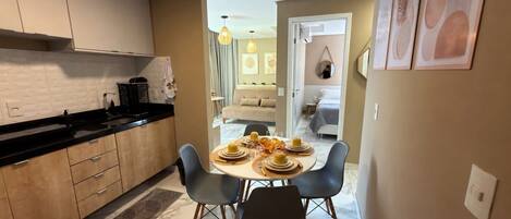 A modern kitchen with a dining area, featuring a round table with chairs, a coffee machine, and a view into the living room.