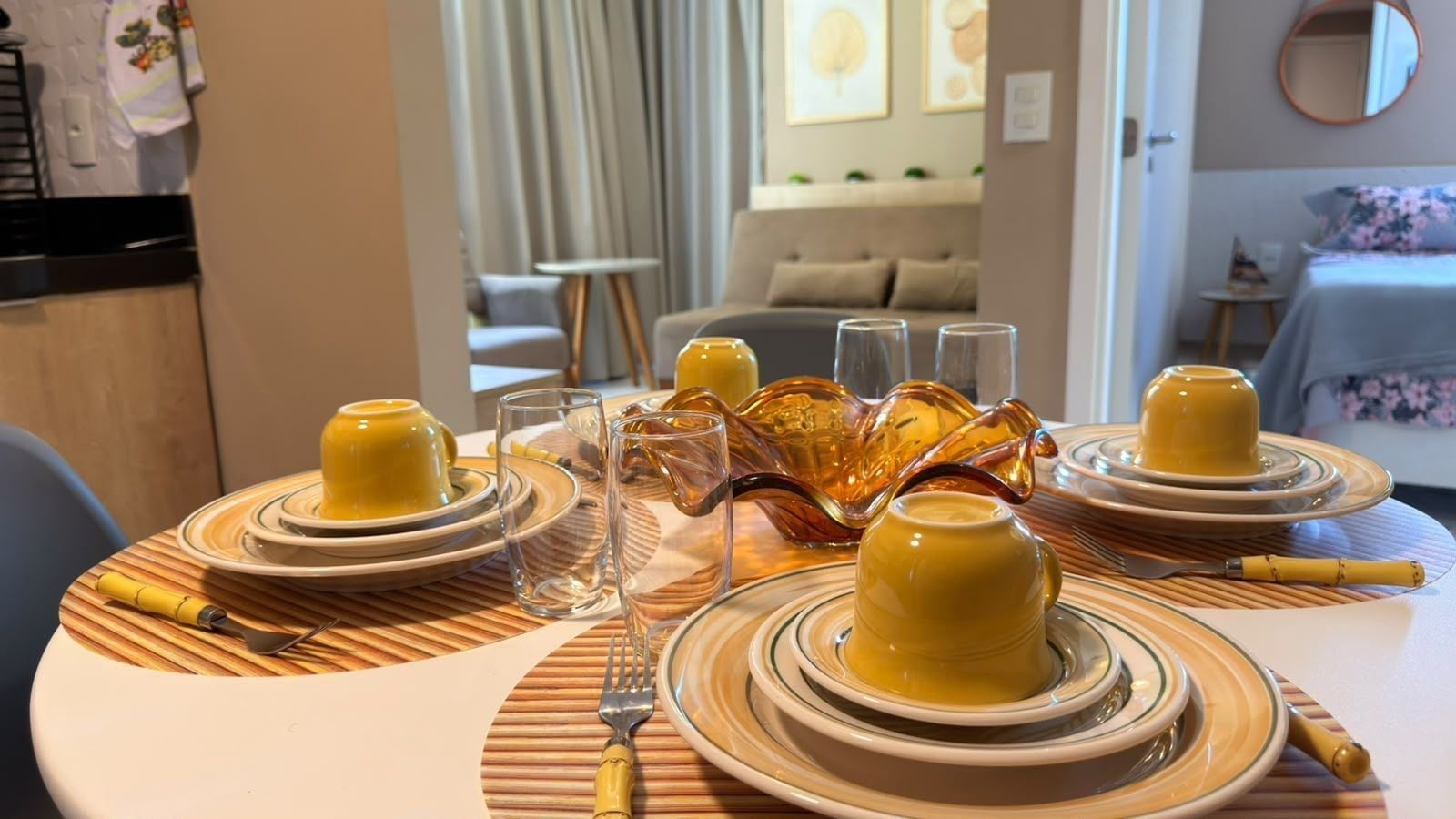 A dining table set with yellow plates, glasses, and cutlery, with a decorative glass bowl centerpiece.