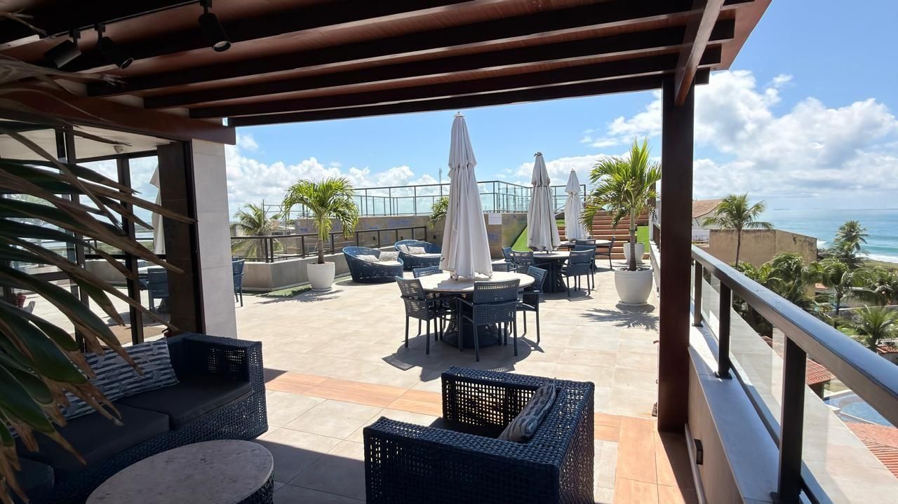 Un patio al aire libre con mobiliario de mimbre, sombrillas y vista al océano.