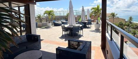 Une terrasse extérieure aménagée avec des meubles en osier, des parasols et une vue sur l’océan.