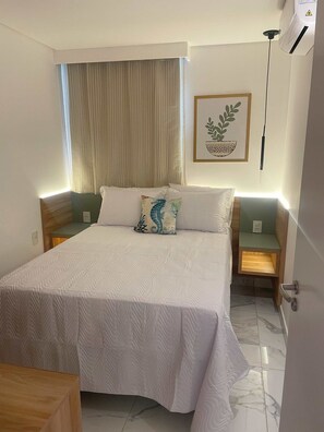 Une chambre à coucher bien rangée, avec un grand lit, une table de chevet, une commode, une fenêtre avec des rideaux et un climatiseur fixé au mur.