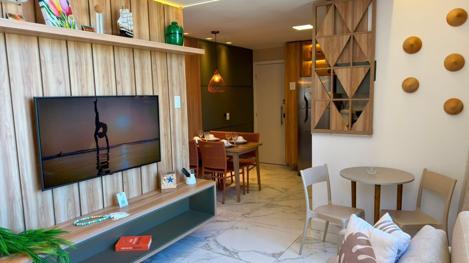 Un salon moderne doté d’un téléviseur à écran plat, d’étagères en bois, d’un coin repas avec des chaises et d’une petite table ronde.