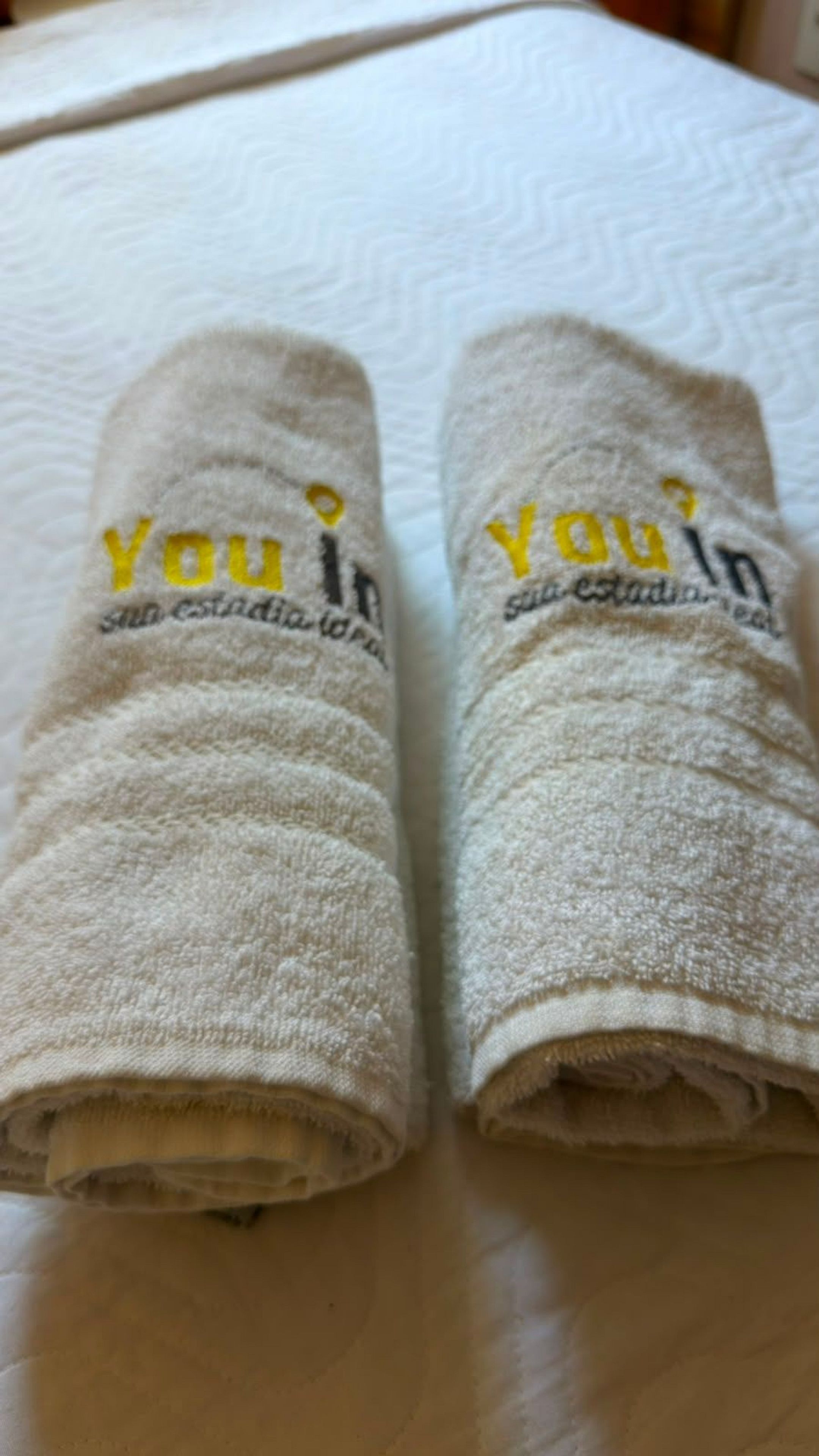 Two rolled towels with embroidered text on a bed.