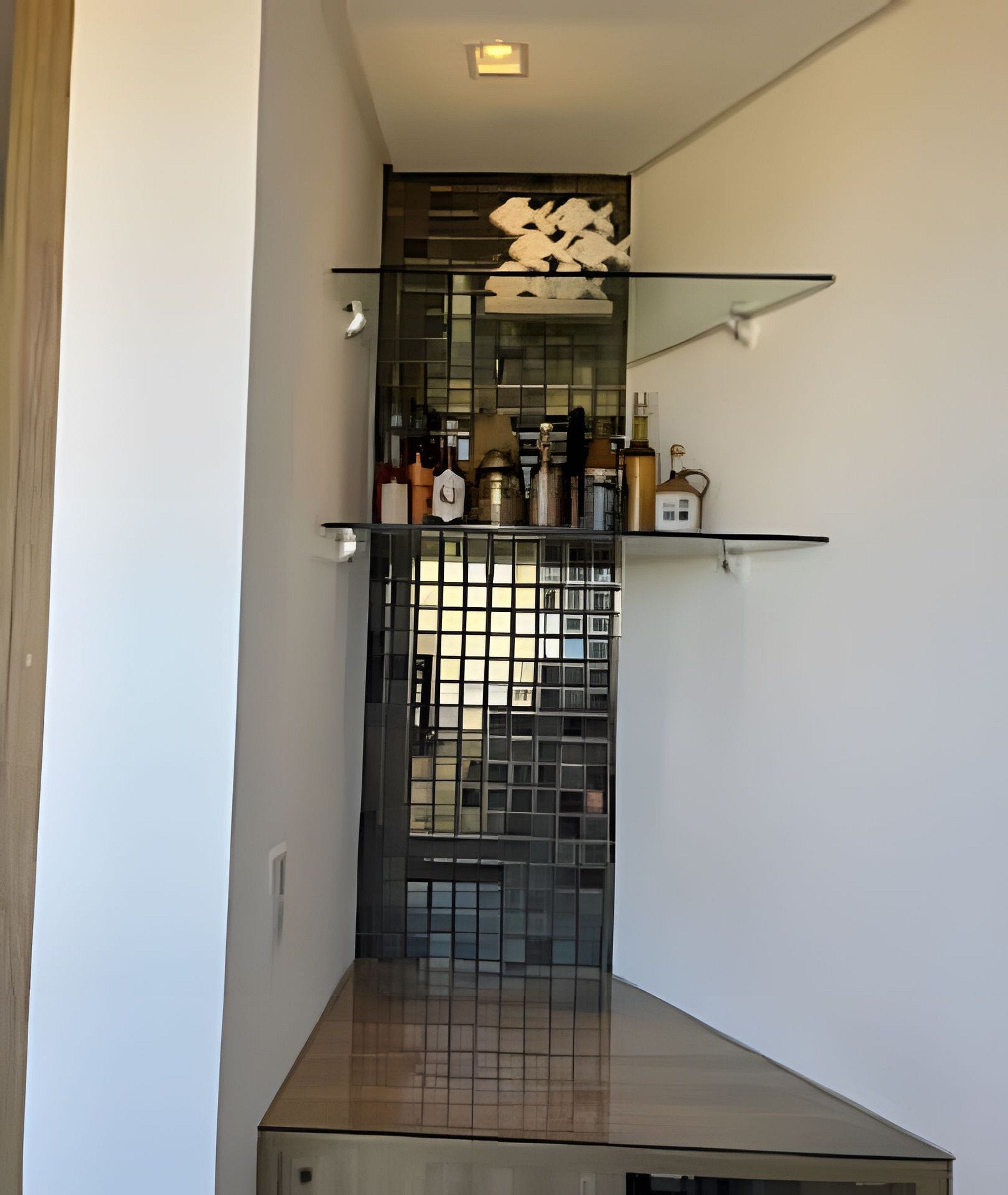 A narrow hallway with a decorative glass partition, a small shelf with bottles, and a tiled floor.
