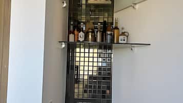 A narrow hallway with a decorative glass partition, a small shelf with bottles, and a tiled floor.