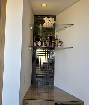 A narrow hallway with a decorative glass partition, a small shelf with bottles, and a tiled floor. - Porto Atlantis (Ipojuca)