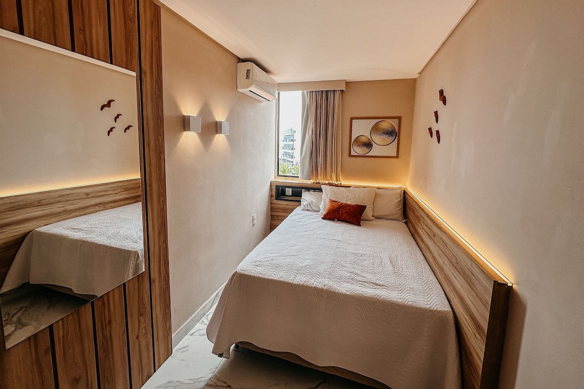 A hotel room with two beds, wooden paneling, a window with curtains, wall-mounted lights, and a painting.