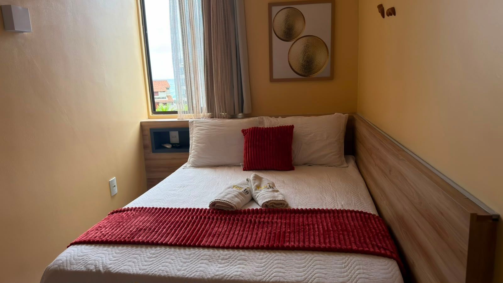 Una habitación de hotel con una cama, una toalla roja y vistas al exterior a través de una ventana.