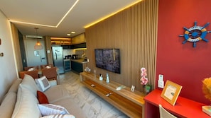 A modern living room with a flat-screen TV, a wooden console table, and a red accent wall. - Porto Atlantis (Ipojuca)