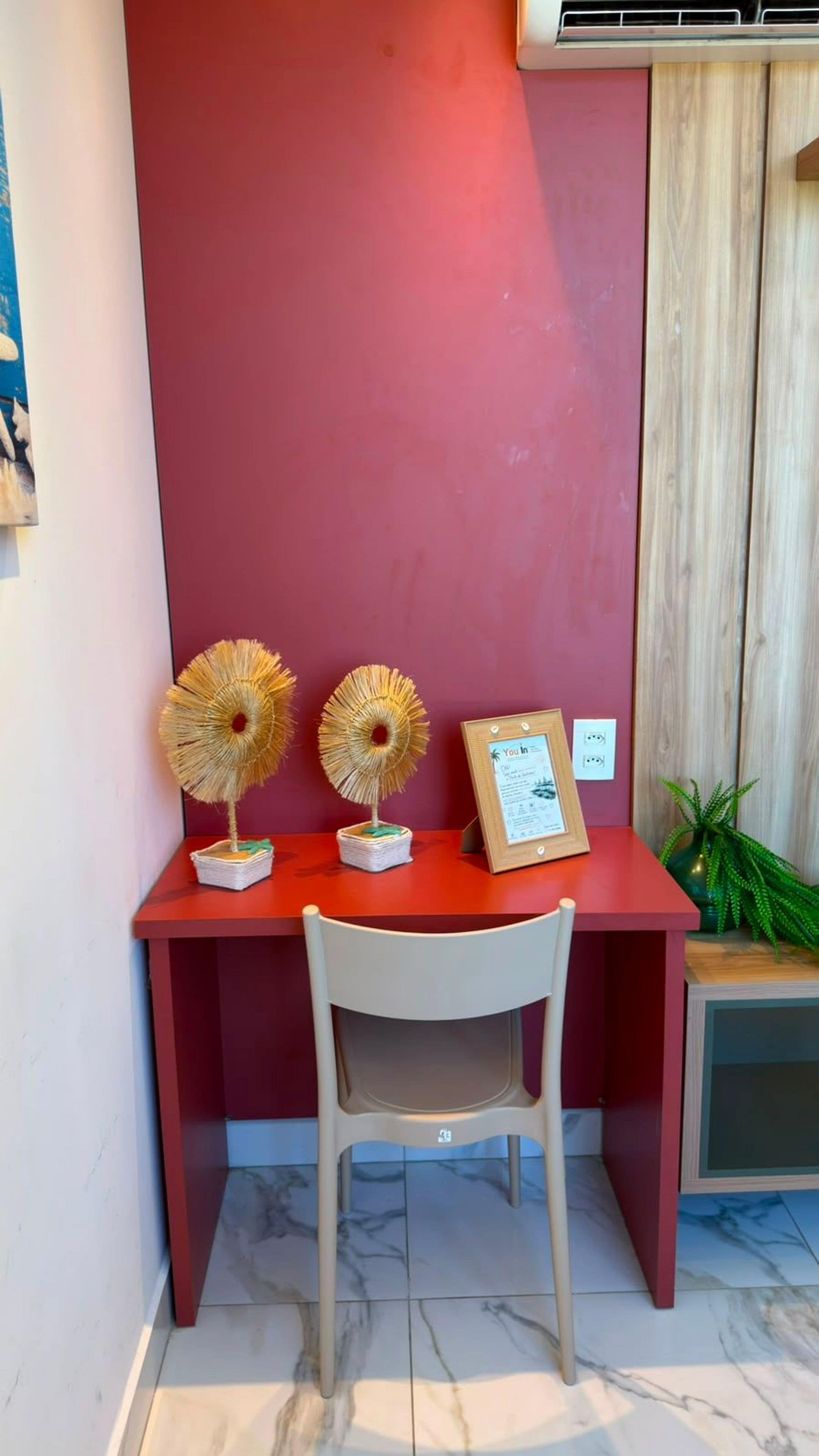 A desk with two decorative fans, a framed certificate, and a chair in front of a red wall.