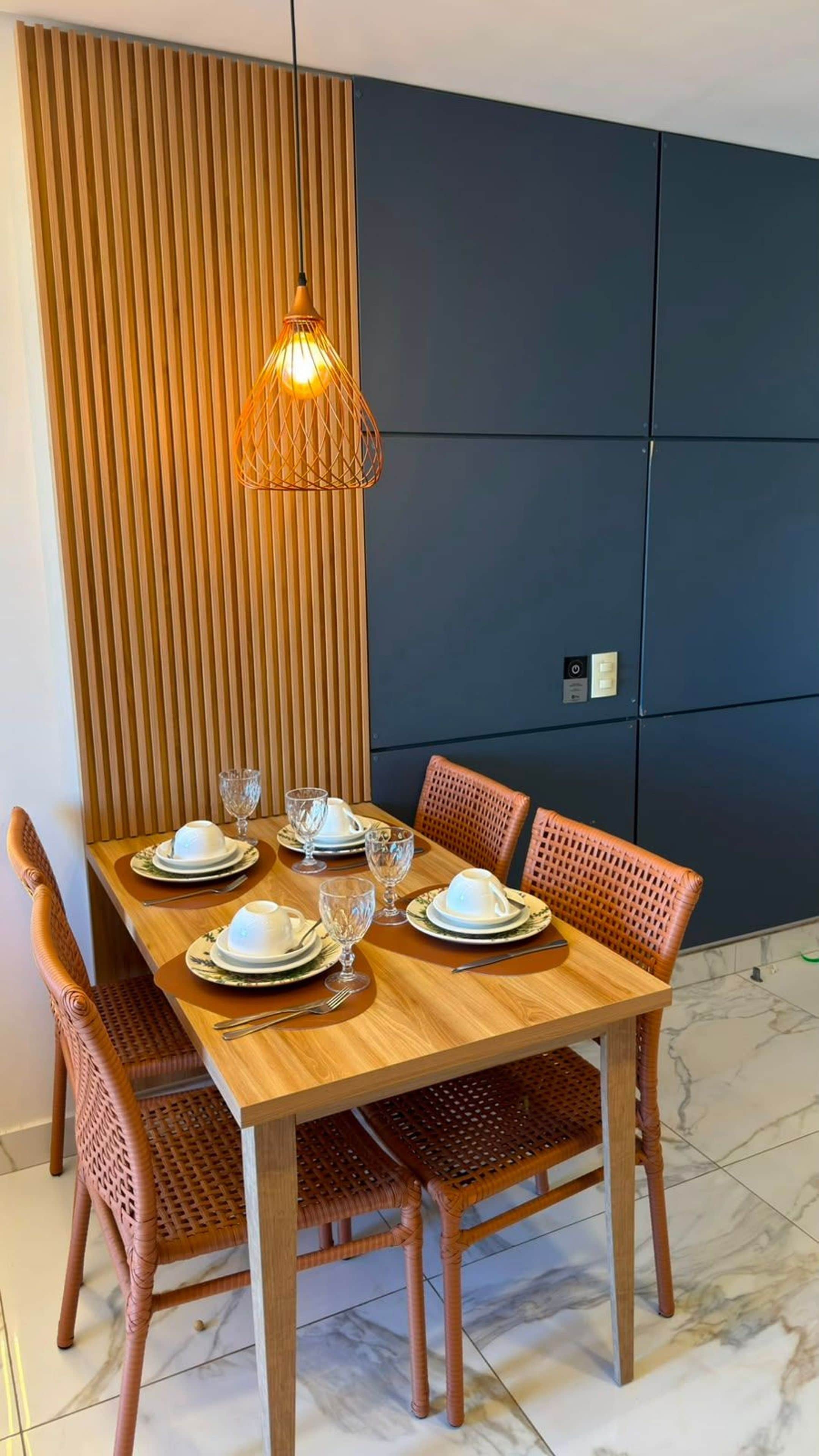 A dining table set with plates, glasses, and cutlery, surrounded by wicker chairs, with a pendant light above.
