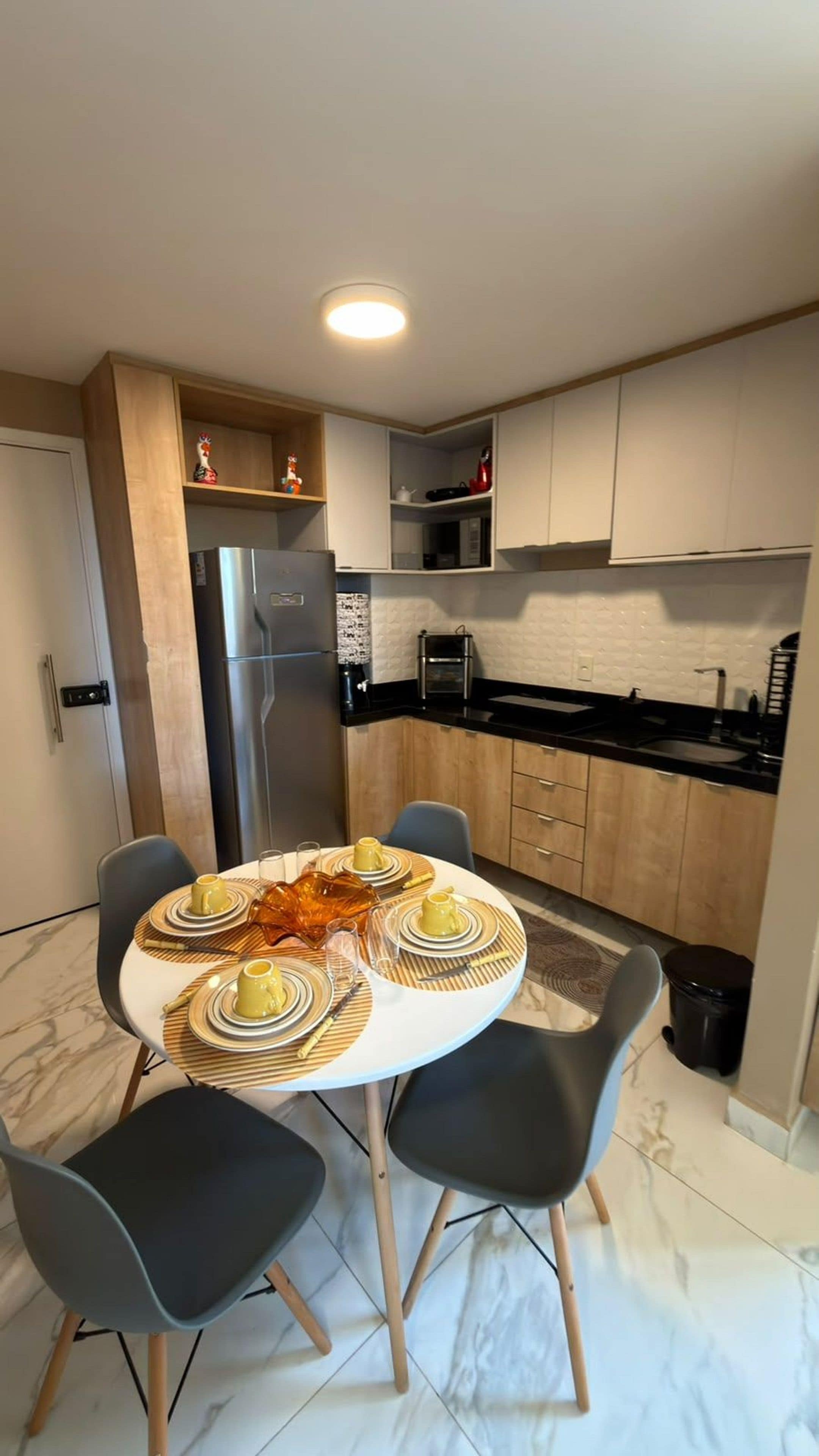 A modern kitchen with a dining area, featuring a round table set for four, a refrigerator, and built-in cabinets.