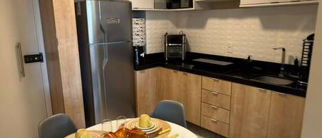 A modern kitchen with a dining area, featuring a round table set for four, a refrigerator, and built-in cabinets.