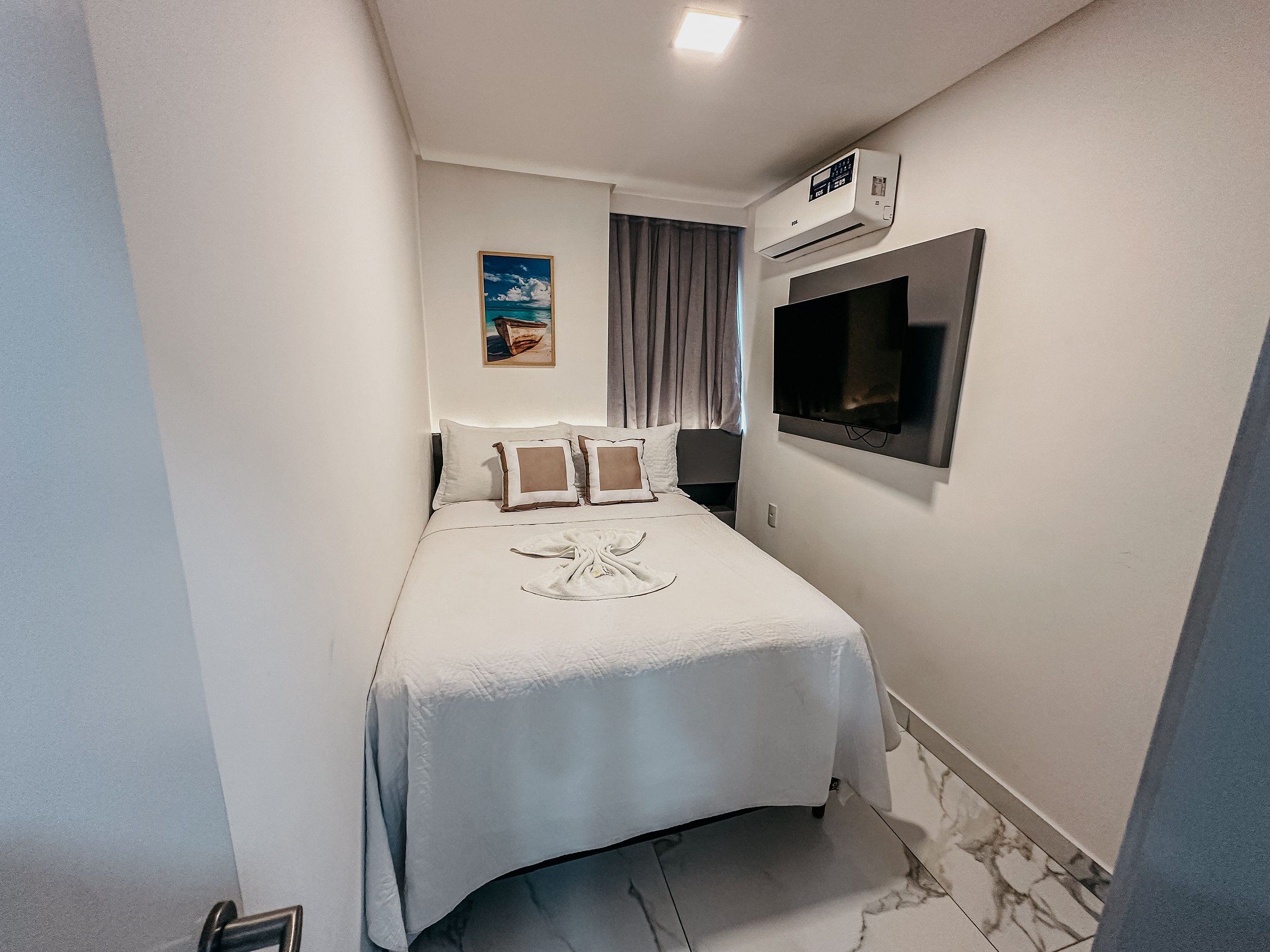 A hotel room with a bed, an air conditioning unit, a flat-screen TV, and a painting on the wall.