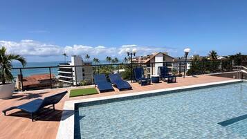 Una piscina en la azotea con sillas de descanso y vista al océano.