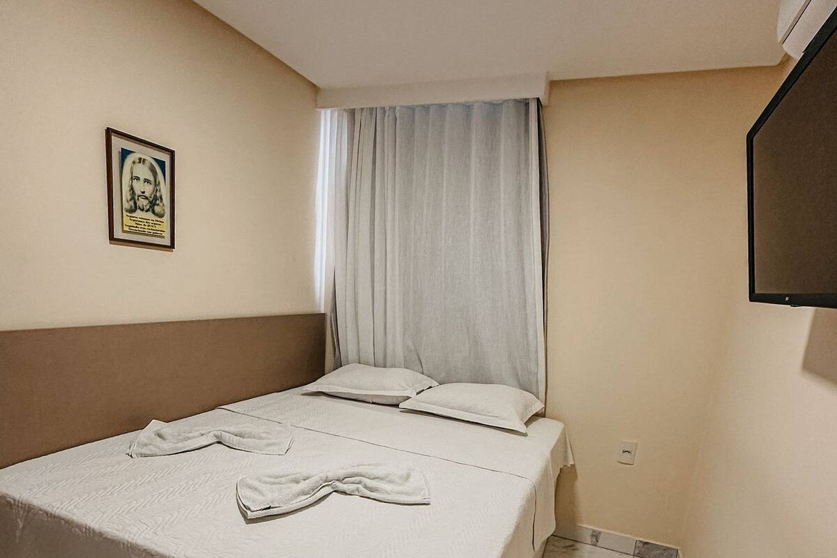 A neatly made bed with a white bedspread and pillows, a framed picture on the wall, and a tiled floor.
