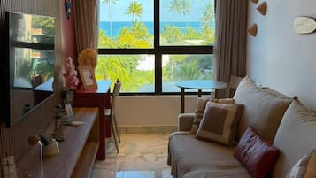 A modern living room with a sofa, a TV, a dining table, and a view of the ocean.