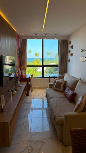 A modern living room with a sofa, a TV, a dining table, and a view of the ocean. - Porto Atlantis (Ipojuca)