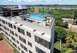 A modern building with a rooftop pool, large windows, and a view of a river and greenery. - Porto Atlantis (Ipojuca)