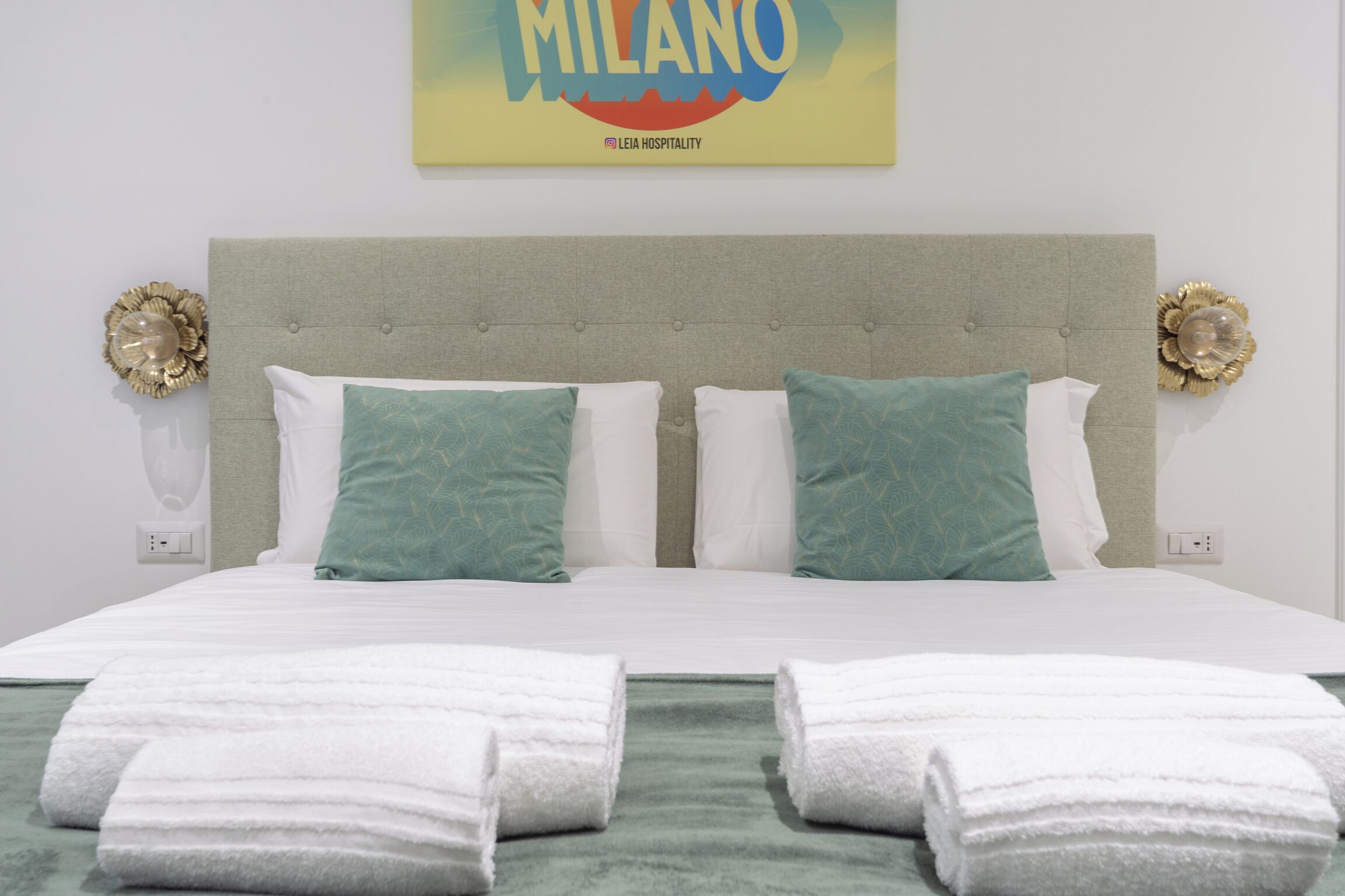 Habitación de hotel con una cama grande, dos almohadas, un cabecero y dos apliques de pared.