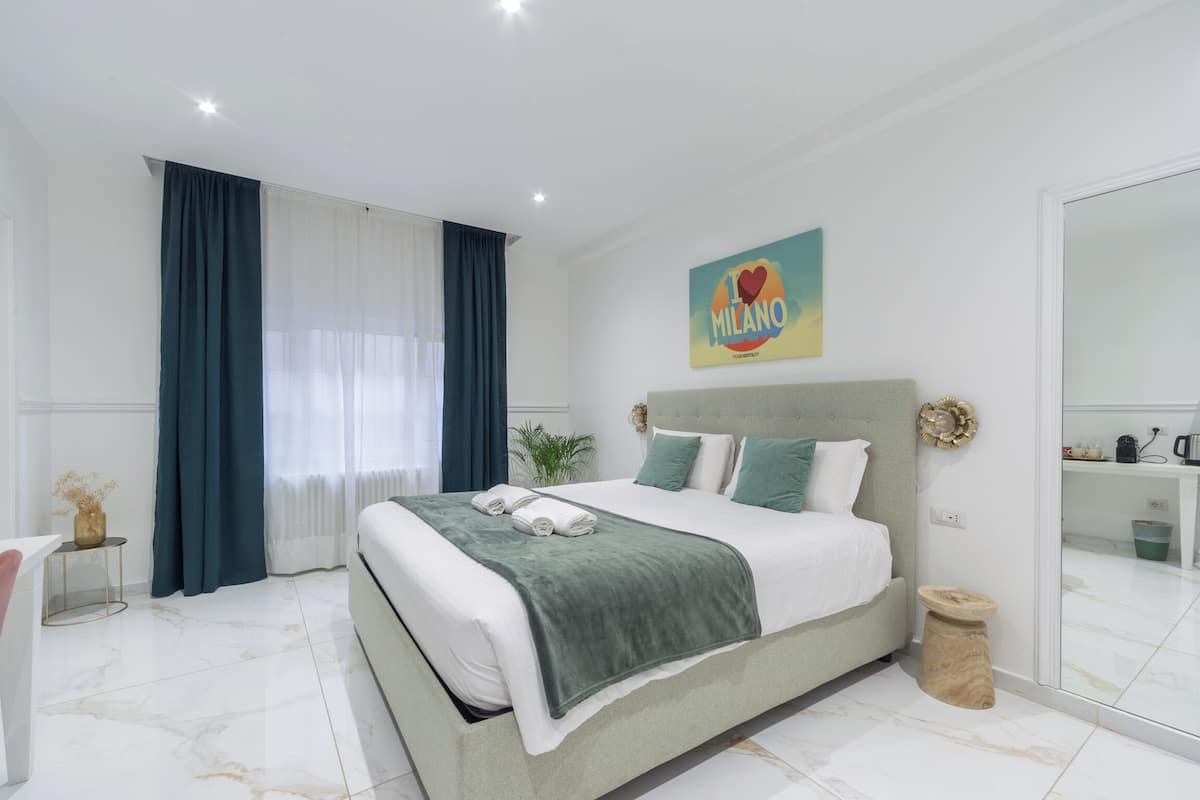 A modern hotel room with a large bed, a bedside table, a mirror, and a view of the bathroom.