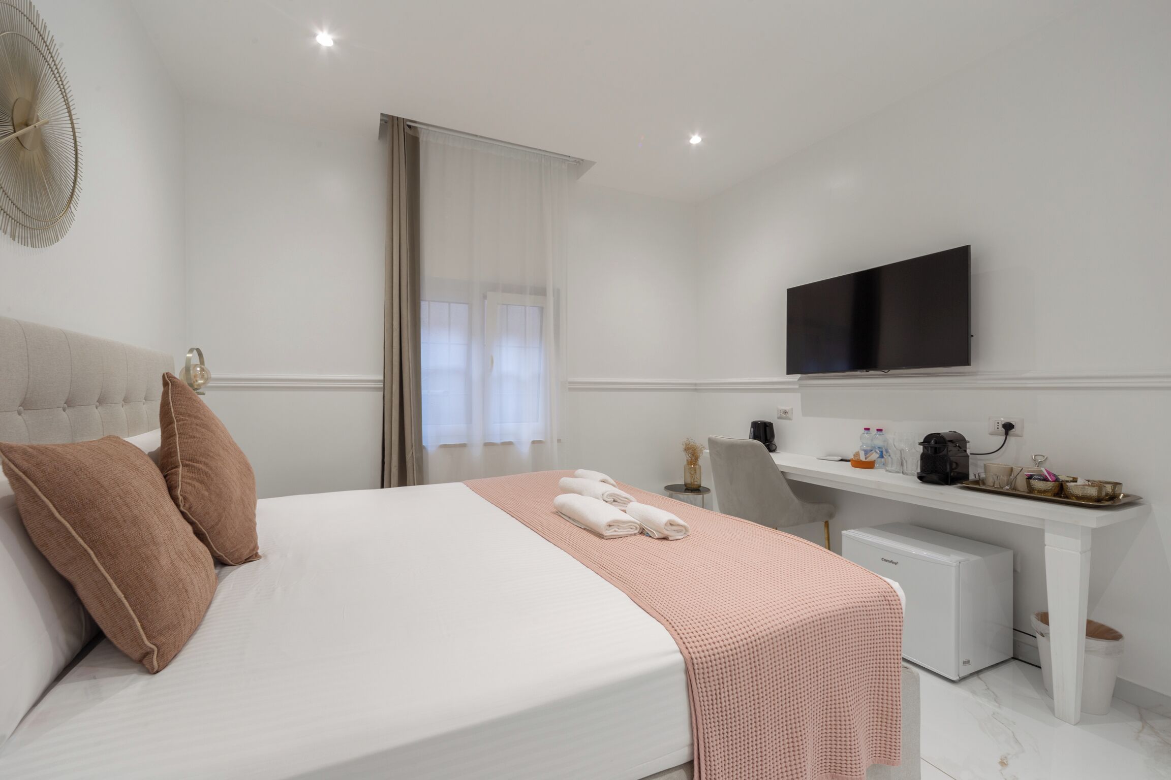 A hotel room with a bed, a desk, a television, and a small kitchenette.