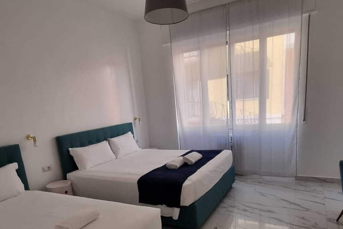 A hotel room with two beds, a large window with sheer curtains, and a marble floor.