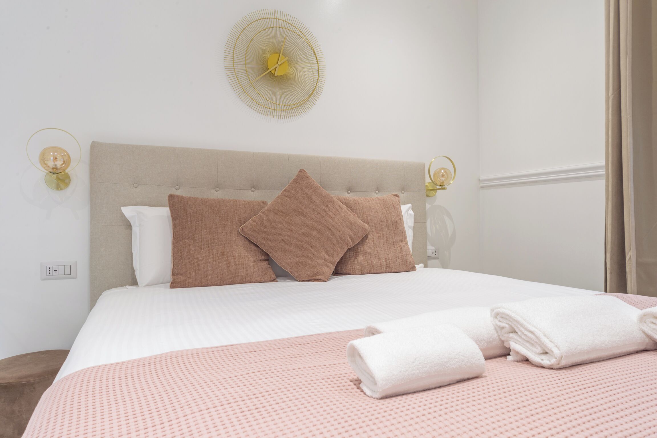 A neatly made bed with a pink and white bedspread, two brown pillows, and a white towel folded on the bed.